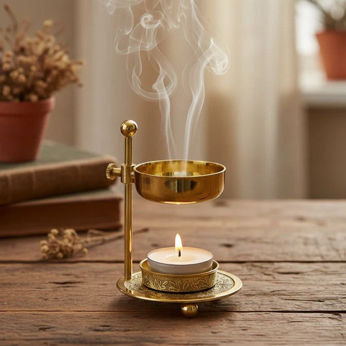 Gold incense burner with a candle on a wooden surface, emitting smoke.