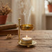 Gold incense burner with a candle on a wooden surface, emitting smoke.