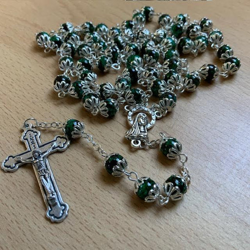 Green rosary with silver cross and Our Lady of Lourdes pendant on a wooden surface