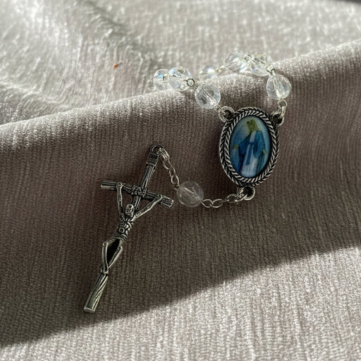 Rosary bracelet with clear beads and religious charm on a textured surface