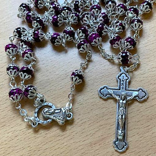 Rosary with purple beads and silver crucifix on a wooden surface