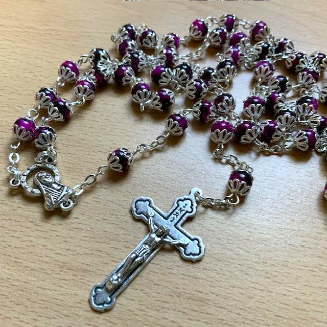 Rosary with purple beads and silver cross on a wooden surface