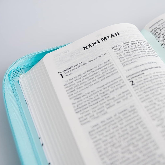 An open Bible or book with the page titled 'NEHEMIAS' resting on a light aqua zippered case, photographed on a clean white background.