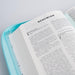 An open Bible or book with the page titled 'NEHEMIAS' resting on a light aqua zippered case, photographed on a clean white background.