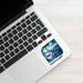 A square sticker with a nautical design is placed on the palm rest of a silver laptop. The sticker features a blue background with a white ship's wheel, a red and white striped lighthouse, and the text 'BE STRONG' and 'God Will Help You Through'.