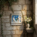 Decorative plaque with religious scene on a stone wall with a vase of flowers.