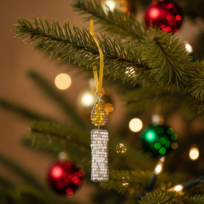 A handmade beaded candle ornament featuring a white beaded candle body and a yellow beaded flame on a silver wire frame, hanging from a yellow ribbon against a white background.