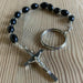 Black beaded rosary with a silver cross on a wooden surface