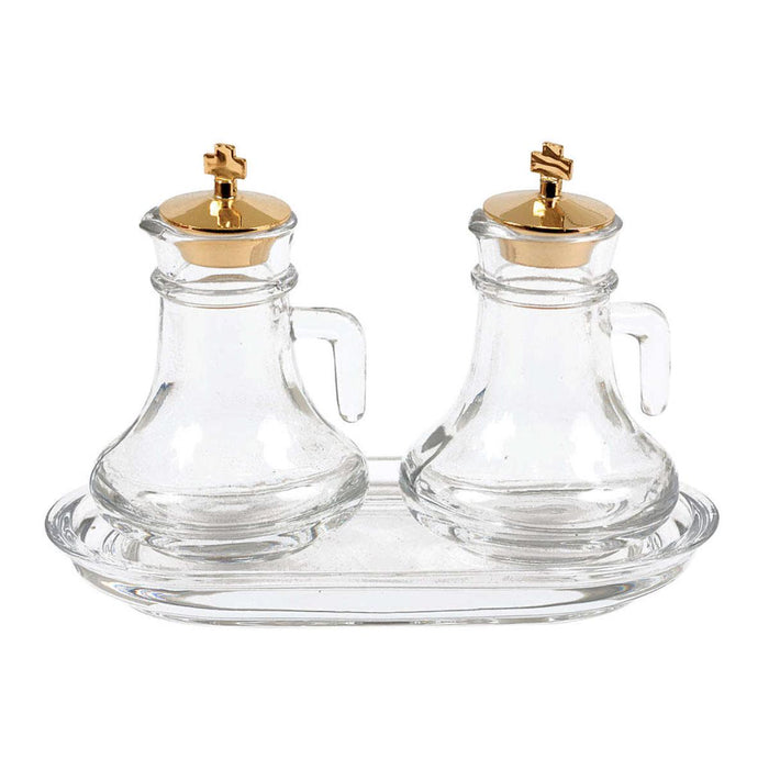 Two clear glass prayer water bottles with gold cross lids, set on a matching clear glass tray against a white background.
