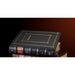A black Holy Bible with gold embossed detailing on the spine and cover, resting on top of other books against a dark brown gradient background.