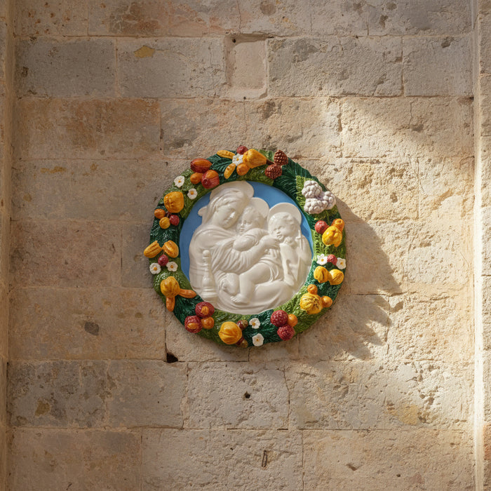 Decorative plate with a central relief of a mother and child surrounded by colorful fruit and flowers.