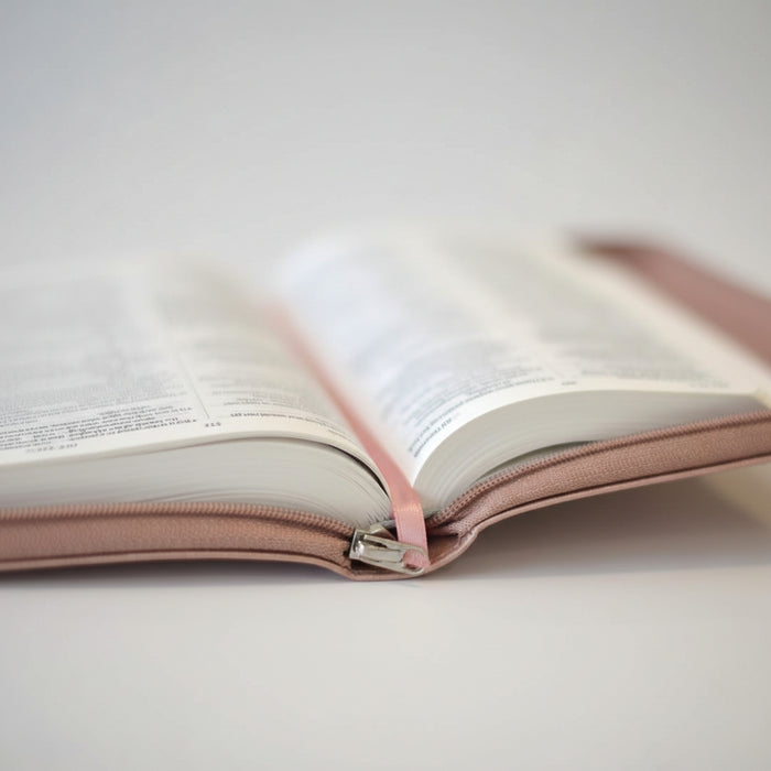 An open book with white pages and a soft blush pink cover, photographed close up on a light neutral surface.