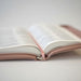 An open book with white pages and a soft blush pink cover, photographed close up on a light neutral surface.