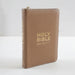 A brown leather Holy Bible with gold foil lettering and a gold zipper, standing upright on a white surface against a light gray background.