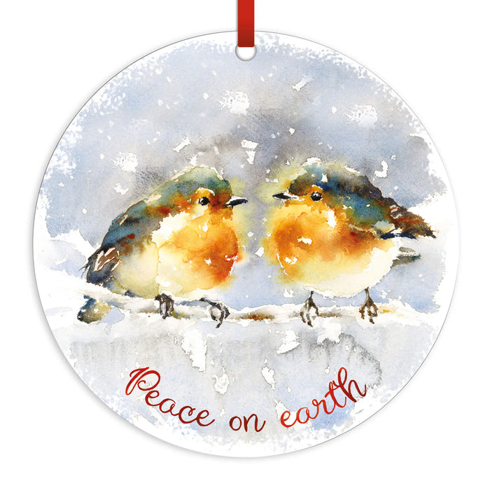 Round hanging ornament with a watercolor painting of two robin birds on a snowy branch and the words 'Peace on earth' in red script. A red hanging ribbon is visible at the top against a plain white background.