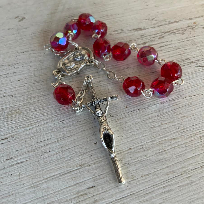 Red beaded rosary with a silver cross on a wooden surface