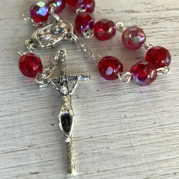 Red beaded rosary with a silver crucifix on a light wooden surface