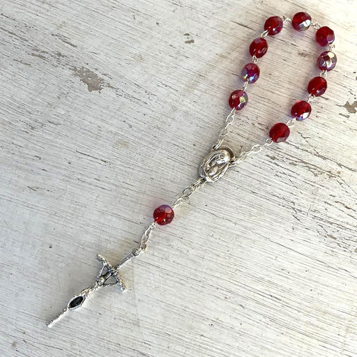 Rosary with red beads and silver cross on a textured surface