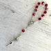 Rosary with red beads and silver cross on a textured surface
