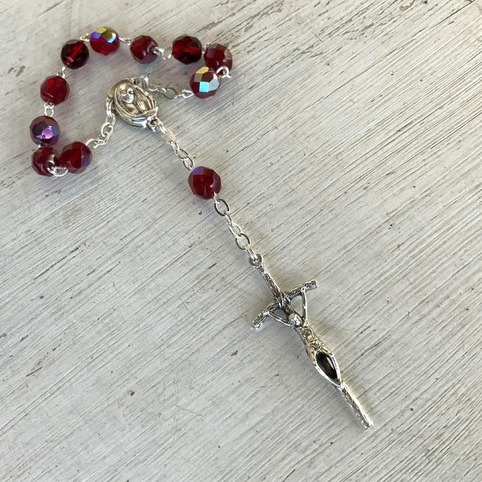Rosary with red beads and silver cross on a light wooden surface