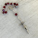 Rosary with red beads and silver cross on a light wooden surface