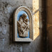 Decorative plaque with a religious scene of a man holding a child against a blue background, framed in beige.