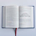 An open book with printed text pages, featuring a prominent title reading 'ST JOSEPH, SPOUSE OF THE BLESSED VIRGIN MARY' on the right page. The book has a dark blue cover visible along the left and right edges, and a red ribbon bookmark hangs from the bottom center.