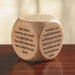 A multicolored wooden prayer cube with different prayers written on each of its six faces, placed on a wooden surface.